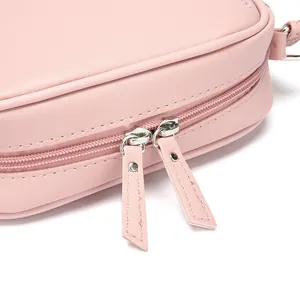 Close-up detail of pink PU leather crossbody bag showing dual zipper and fine texture
