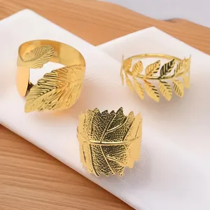 Close-up of three different golden leaf-shaped metal napkin rings with intricate textures