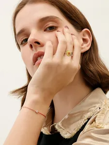Nahaufnahme eines eleganten Sonnenblumenrings und eines zarten roten Armbands an einem Modell