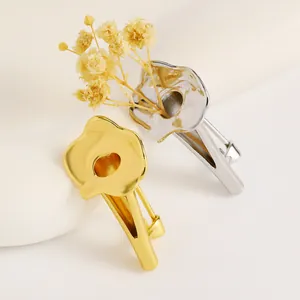 Detailed shot of creative vase-shaped brooches in gold and silver with dried flowers.