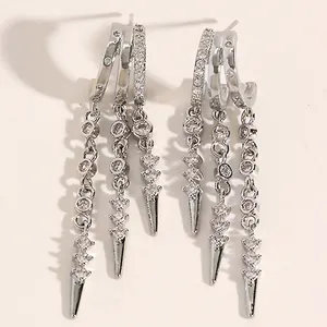 Close-up of silver-tone hoop earrings with dangling zircon chains and spike charms.