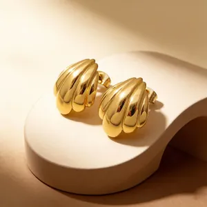 Vista macro di orecchini a conchiglia in acciaio dorato su un supporto beige caldo