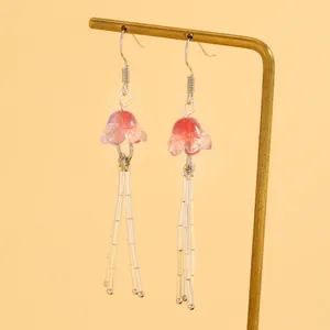 Gros plan de boucles d'oreilles méduses roses avec glands en perles sur support doré