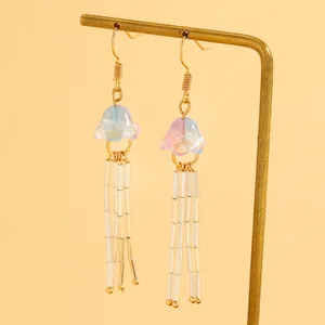 Détail de boucles d'oreilles méduses à glands dégradés rose et bleu sur support doré