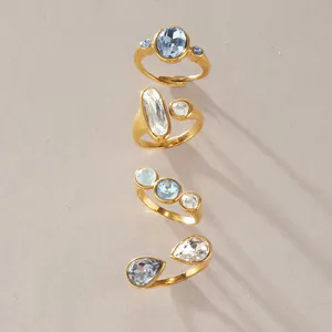 Detailansicht von vier eleganten vergoldeten Edelstahlringen mit blauen und klaren Kristallen.