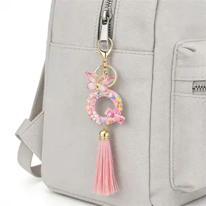 Heart sequin letter Q keychain with pink butterfly charm and tassel on a grey bag.