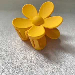 Vue détaillée d'une pince à cheveux en forme de fleur jaune mat sur fond texturé blanc