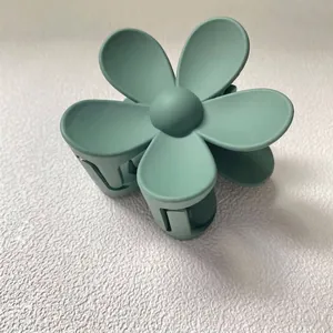 Détail rapproché d'une pince à cheveux en forme de fleur vert mat sur fond texturé