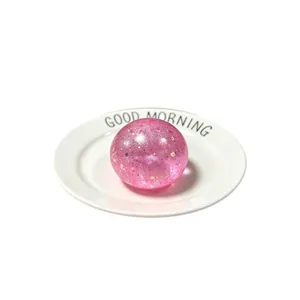 Pink glitter maltose syrup stress relief squishy ball toy on white ceramic plate