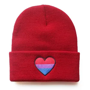 Warm red knitted beanie hat featuring a vibrant bisexual pride flag embroidered heart