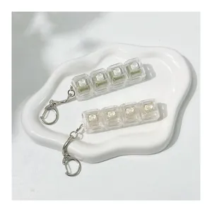 Close-up of two transparent 4-key mechanical keyboard switch tester keychains on a white tray