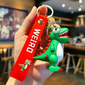 Vue détaillée d'un mignon porte-clés dinosaure en PVC vert tenu en hand avec sangle rouge.