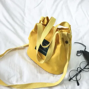 Close-up view of a minimalist yellow canvas bucket bag featuring an artistic letter patch