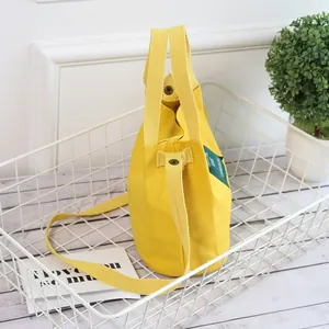 Minimalist yellow canvas bucket bag with handles and shoulder strap in a white basket