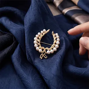 Elegant gold wreath brooch with white pearls on a textured navy blue silk fabric background