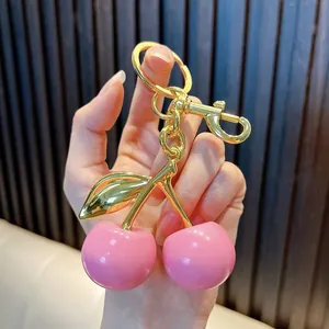 Close-up of a hand holding an elegant pink cherry keychain with polished gold hardware