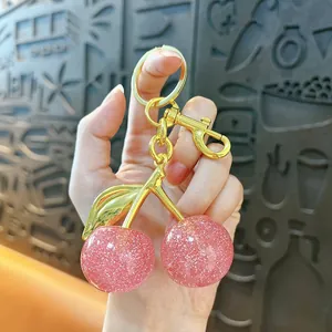Detail view of a pink glitter cherry keychain held in hand as an elegant bag charm accessory