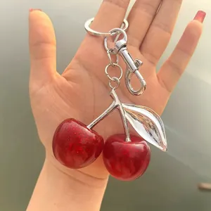 Close-up detail of a sparkling red cherry keychain with silver-toned leaf and metal ring.