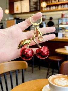 Detailed close-up of a glossy red cherry keychain charm with elegant golden leaves