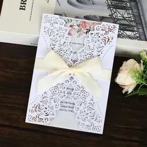 Close-up of elegant white laser-cut bridal shower invitation with a cream ribbon bow