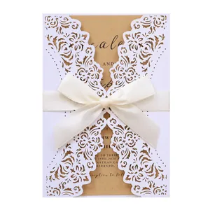 Detail of white laser-cut wedding invitation with cream ribbon and kraft inner card.