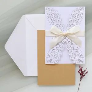 Elegant white laser-cut wedding invitation set with cream ribbon bow and kraft card