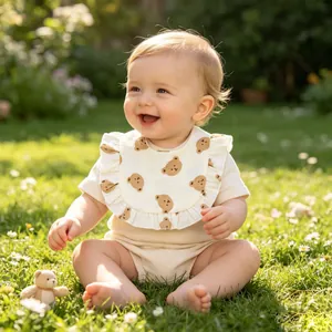 Cute baby wearing a ruffled cotton gauze bib with bear print in a sunny garden setting