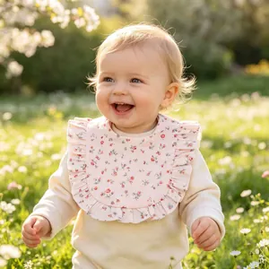 Detailed view of a baby girl wearing a delicate floral ruffled cotton bib in a sunny garden