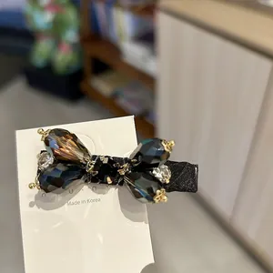 Close-up detail of an elegant black rhinestone bow hair clip featuring luxury gold metal accents