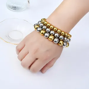 Close-up of a hand wearing three stacked gold and silver stainless steel beaded bracelets