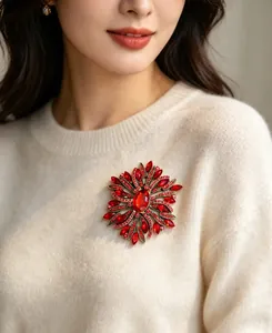 Macro detail view of a large red crystal flower brooch pinned on a cream wool sweater.