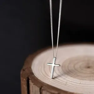 Close-up of minimalist S925 sterling silver cross pendant necklace on wood stand
