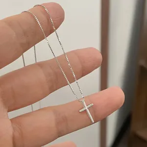 Detailed macro view of a sterling silver cross pendant on a classic box chain held by hand.