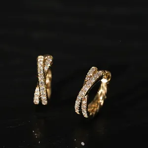 Nahaufnahme eleganter goldener Creolen in Kreuzform mit funkelnden Zirkonia