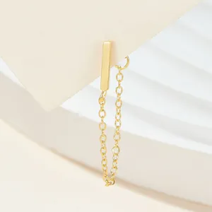 Close-up view of a minimalist gold bar stud earring with a dangling tassel chain.