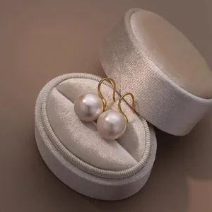 Close-up view of round white pearl ear hooks resting on a luxury velvet jewelry box