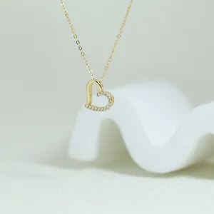 Close-up of a gold heart pendant necklace with pave crystal details on white prop