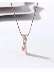 Détail en gros plan du collier pendentif en X or rose avec incrustation de cristaux.