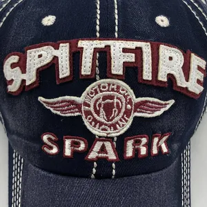 Macro detail van SPITFIRE en SPARK borduurwerk op een marineblauwe gewassen katoenen pet