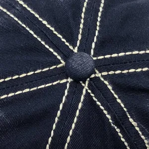 Macro-detail van beige contraststiksels en knop op een marineblauwe gewassen katoenen pet