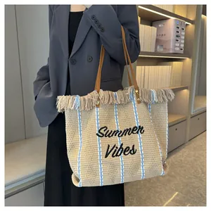 Dettaglio di una borsa da spiaggia intrecciata con ricamo Summer Vibes e decori frange