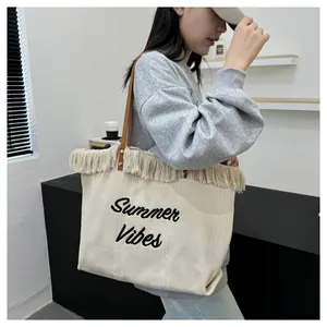 Dettaglio di borsa tote in tela con ricamo Summer Vibes e decorazione a frange.