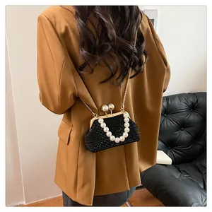 Close-up of black shell-shaped crossbody bag with pearl handle and golden chain