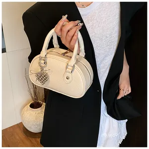 Nahaufnahme der eleganten cremefarbenen Bowlingtasche mit Kieselstruktur und Anhänger