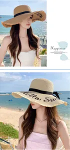 Close-up of a stylish wide brim straw sun hat with 'Hello Sun' embroidery on the beach.