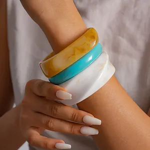 Close-up van model met retro hars gemarmerde armbanden in de kleuren geel, blauw en wit