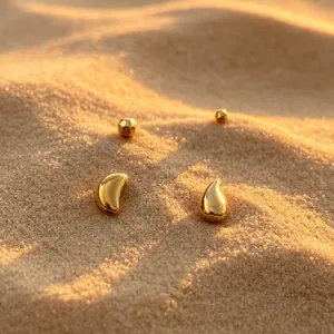 Detailed view of golden vacuum-plated stainless steel teardrop and bean beads on sand