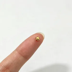 Macro view of a tiny golden faceted stainless steel spacer bead on a fingertip for scale
