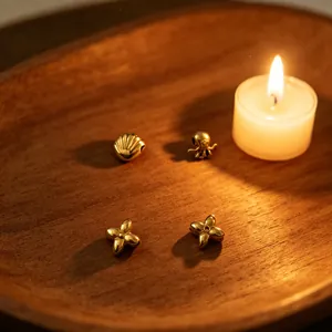 Gold stainless steel beads in shell and octopus shapes on a wooden tray with a candle