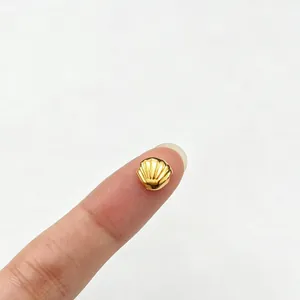 Detailed view of a tiny gold shell spacer bead on a fingertip showing its small scale